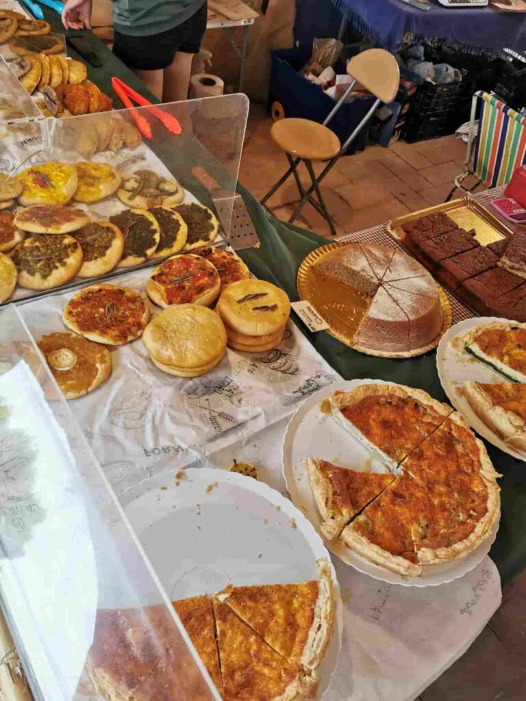 A stall in the market del riurau showing Catalan pizzas called Cocas, and a Bizcocho cake with one slice missing. There are also other cakes with a few slices missing.